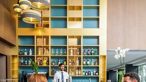 A bar area with a bartender, a counter with various bottles, and a seating area with two chairs and a table. - Novotel Malta Sliema (Gzira)