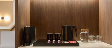 A compact kitchen with a coffee maker, kettle, and tea set on a marble countertop.