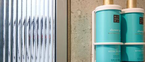 Un baño con ventana, un perchero con dos botellas de gel de ducha y champú Rituals Karma, y una pared con textura.
