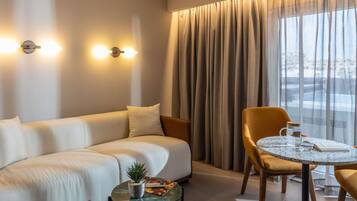 A modern hotel room with a sofa, a round table, a chair, a small potted plant, and a city view.