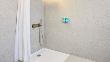 A shower area with a white curtain, a handheld showerhead, and two blue bottles on the wall.