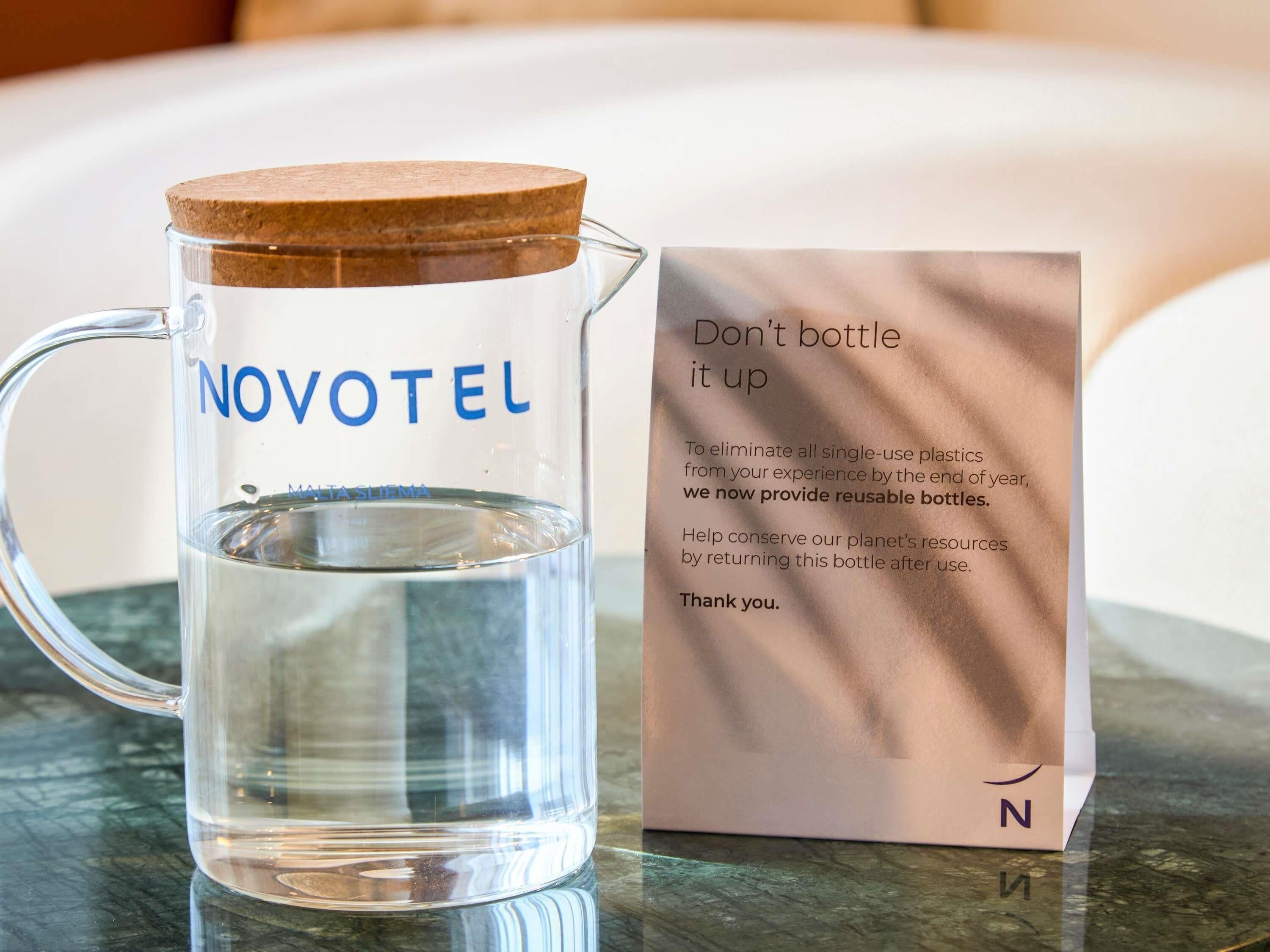 A clear glass water jug with a cork lid and a message card beside it.