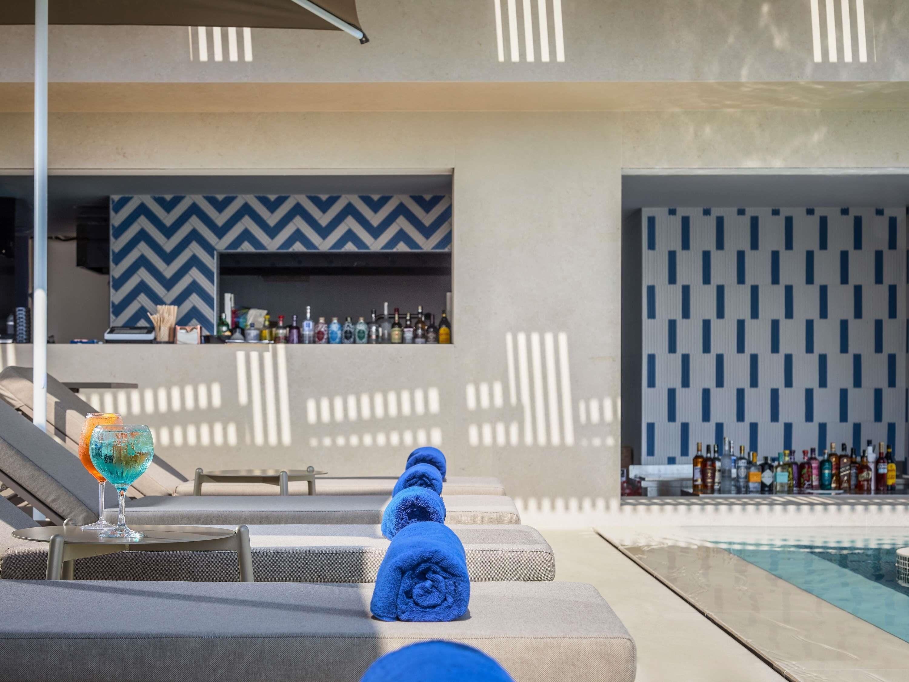 Ein Poolbereich mit Liegestühlen, einer Bar mit Flaschen und einer Wand mit Muster.