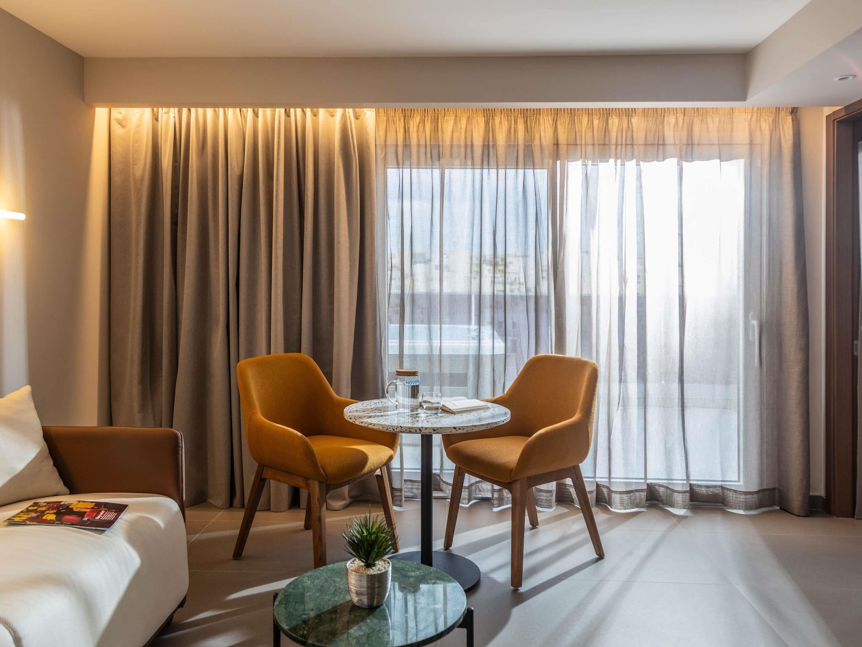 A hotel room with a sofa, two armchairs, a small round table, and a potted plant.