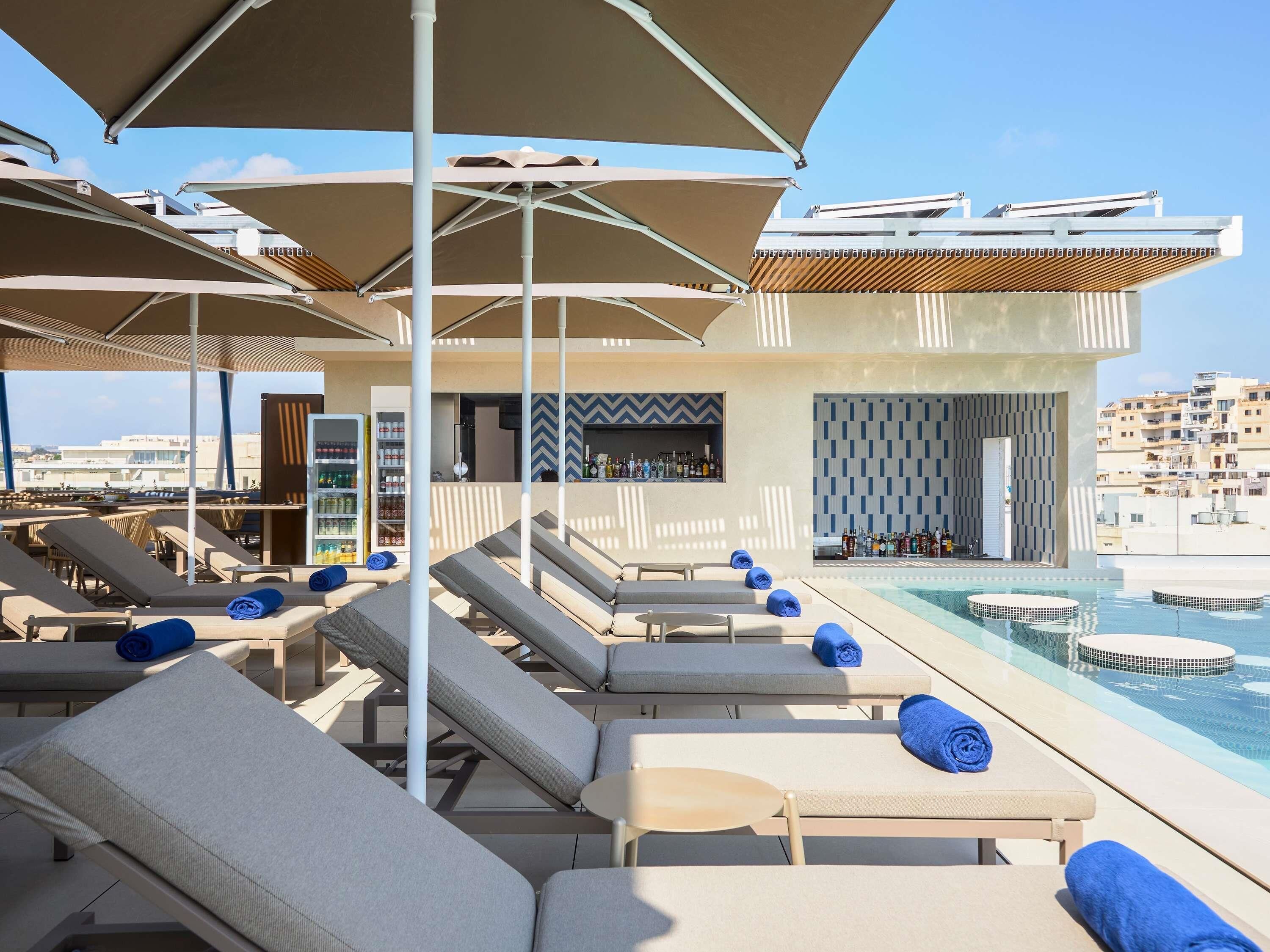 A rooftop pool area with lounge chairs, umbrellas, and a bar.
