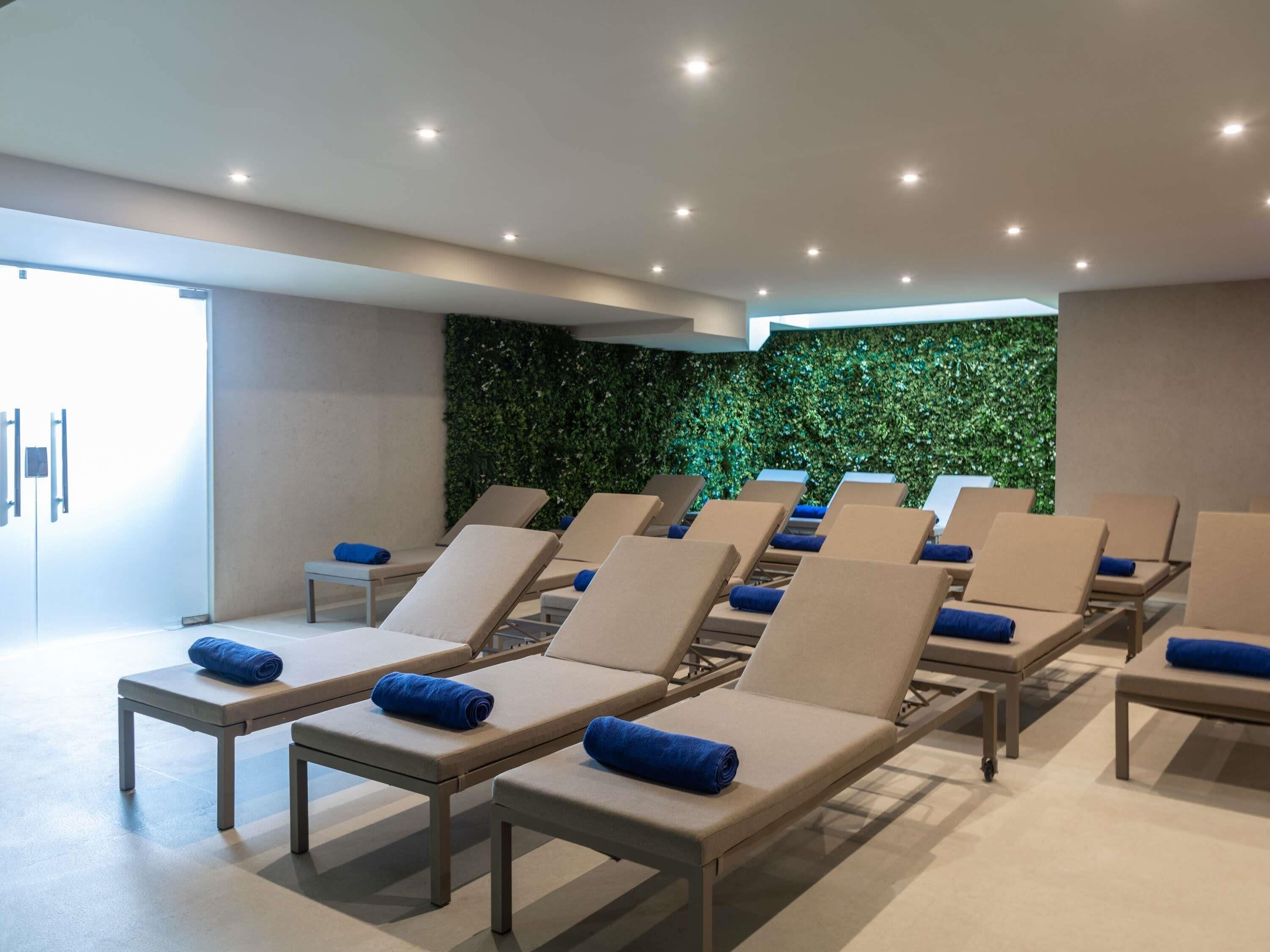 Ein moderner Spa-Bereich mit mehreren Liegen, einer grünen Wand und indirekter Beleuchtung.