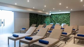 Ein moderner Spa-Bereich mit mehreren Liegen, einer grünen Wand und indirekter Beleuchtung.