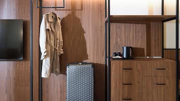 Una habitación moderna con un armario de madera, un perchero, una maleta y un televisor de pantalla plana.