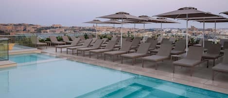 Una piscina sul tetto con poltrone a sdraio e ombrelloni, con vista sulla città.