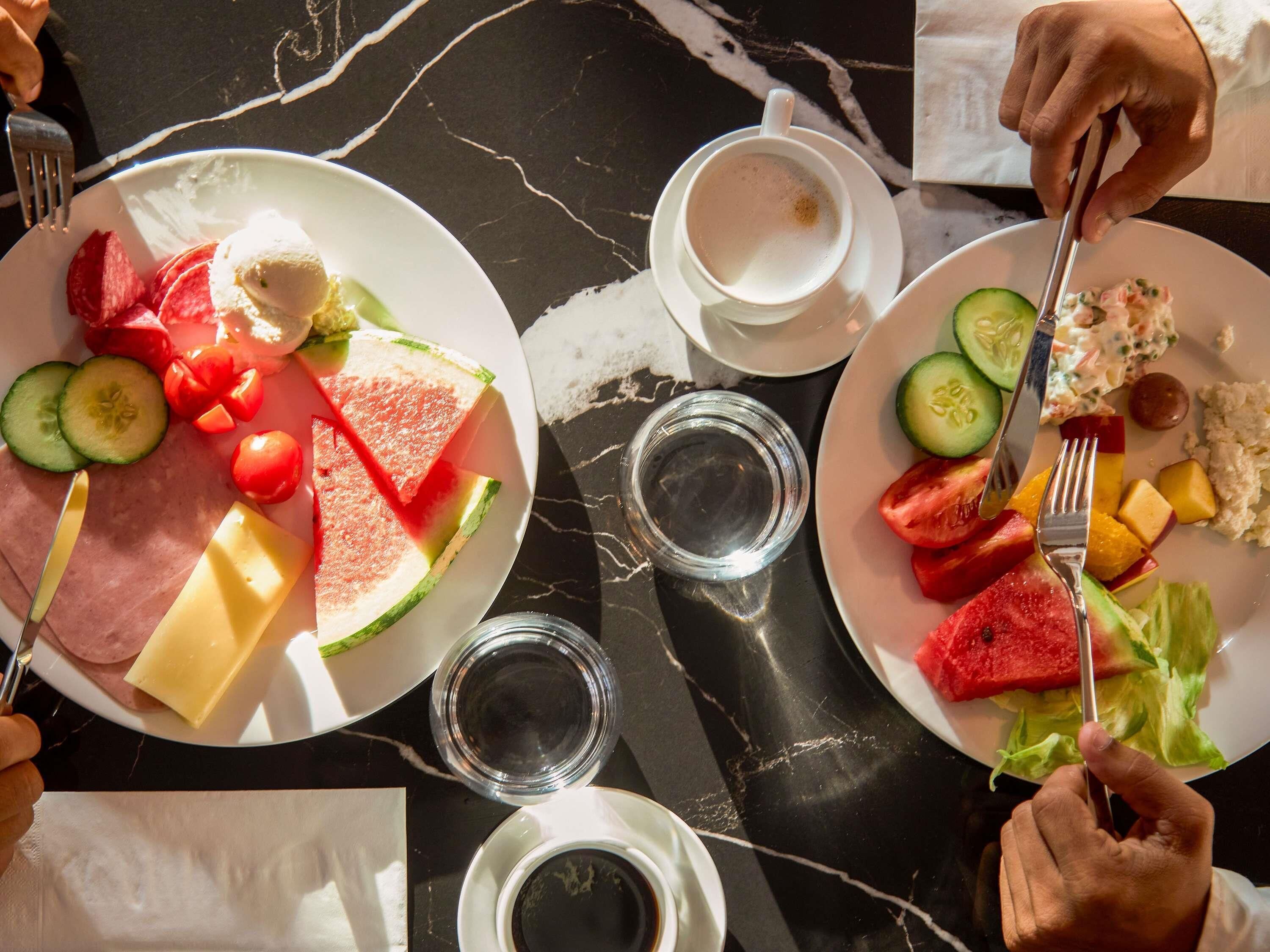 Una mesa de comedor con platos de comida, incluyendo sandía, queso y ensalada, además de dos tazas de café.