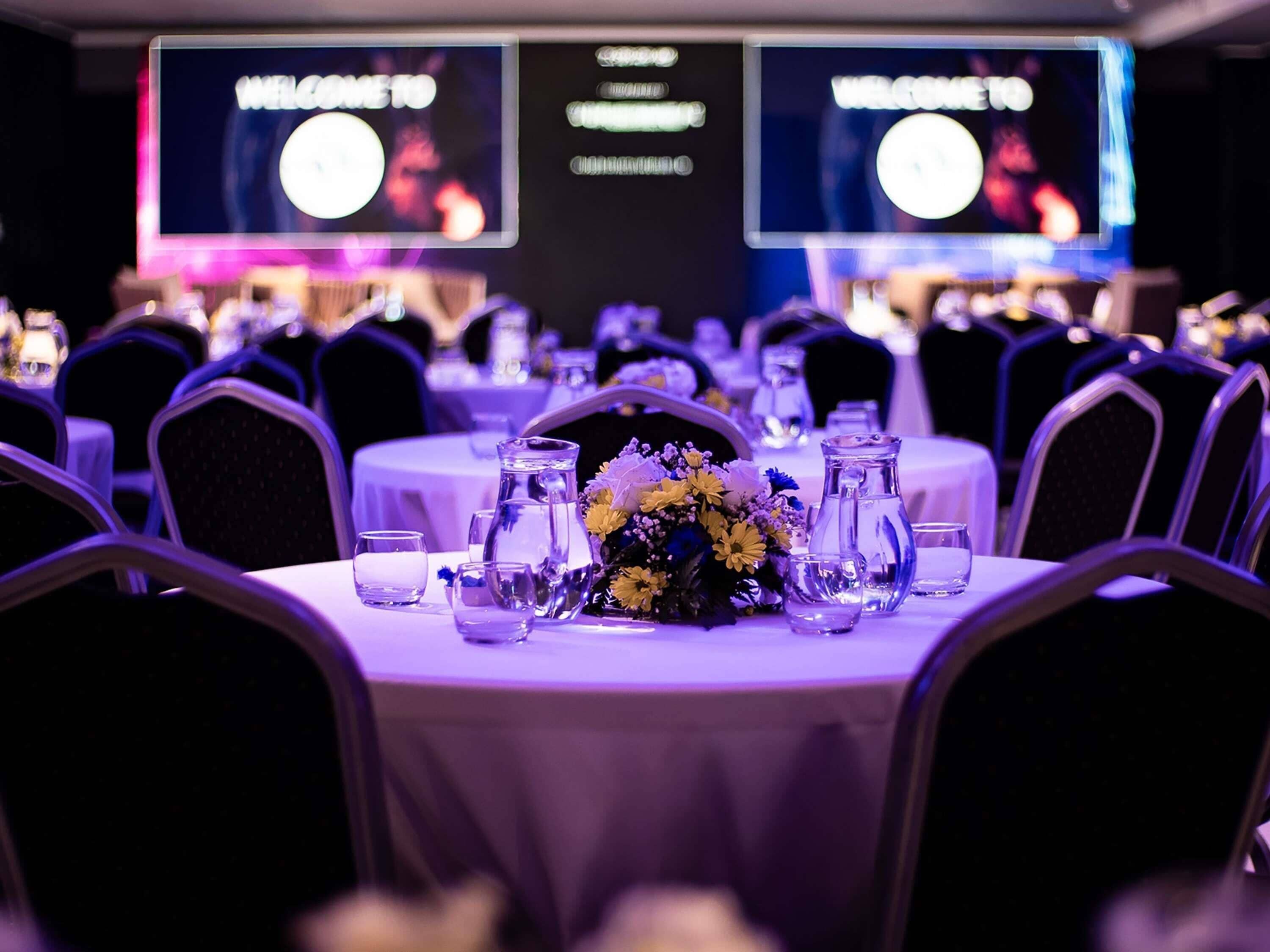 A banquet hall with round tables, chairs, and a floral centerpiece.
