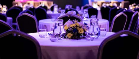 Un salón de banquetes con mesas redondas, sillas y un centro de mesa floral.