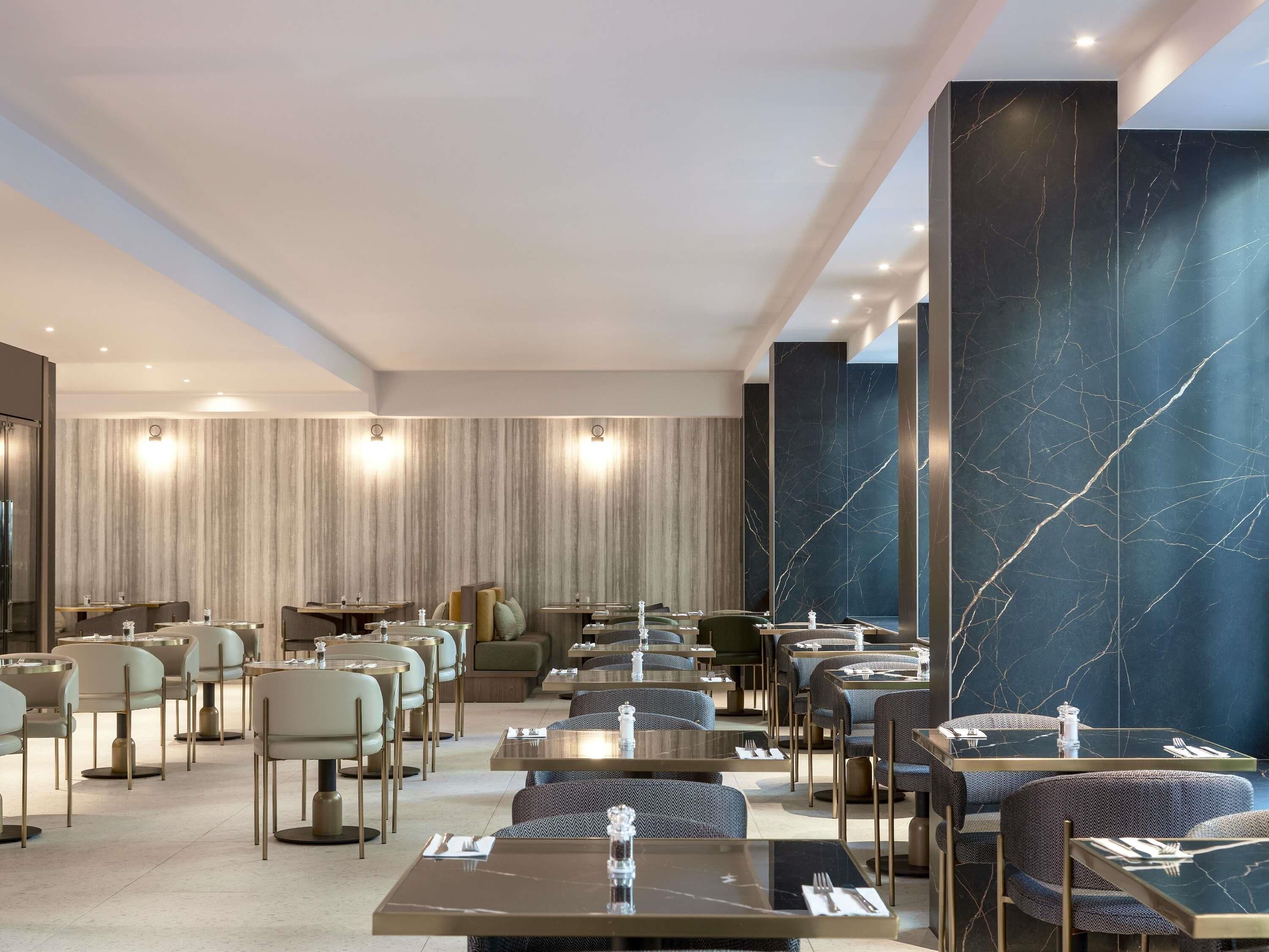 A modern restaurant with marble walls, multiple seating areas, and a clean, contemporary design.