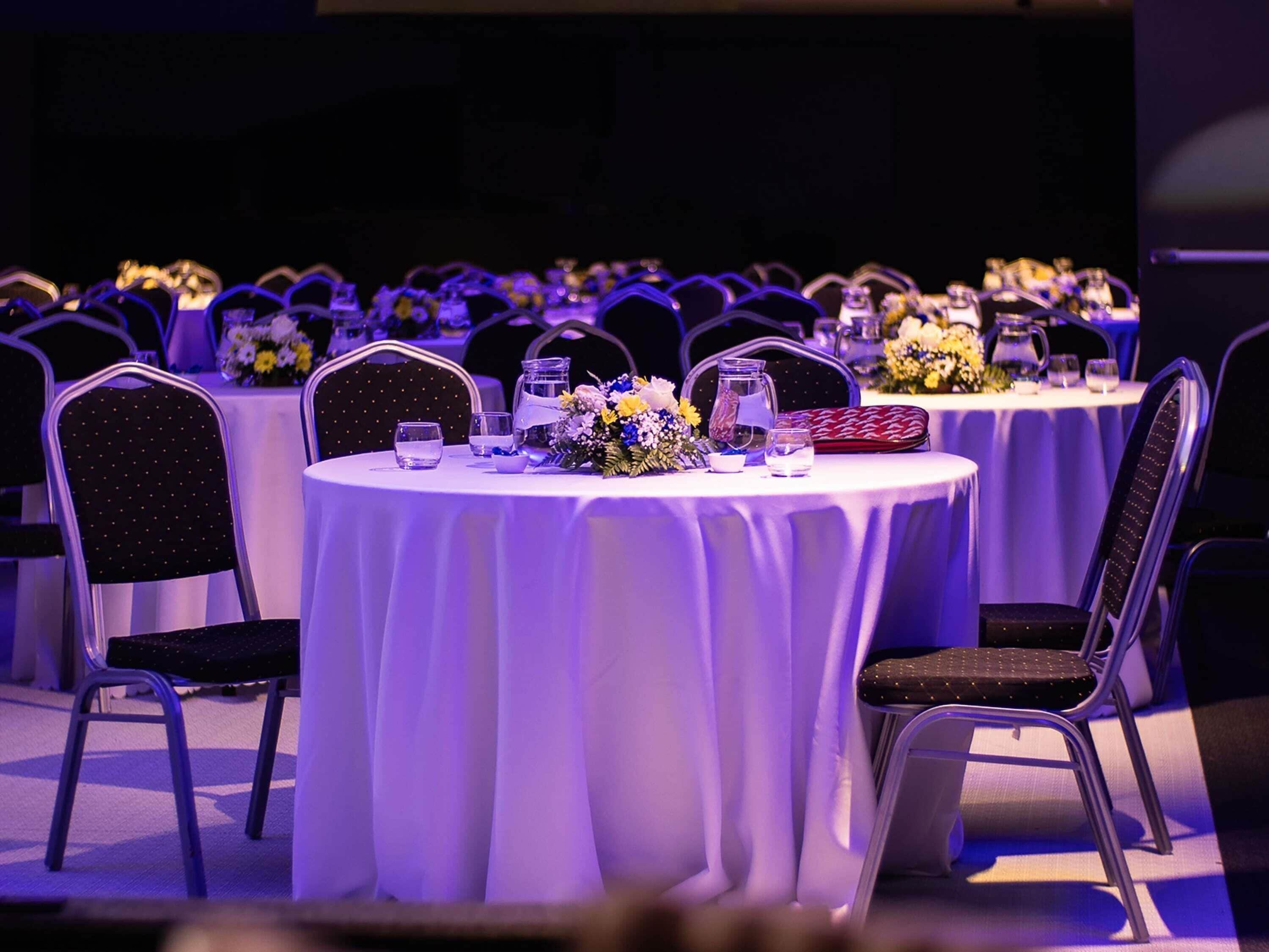 Un salón de banquetes con mesas redondas, sillas y centros de mesa florales.