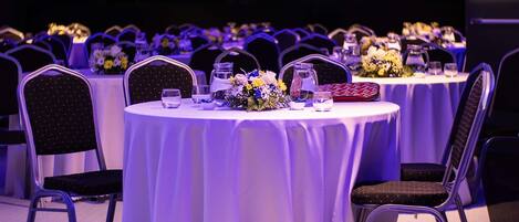Un salón de banquetes con mesas redondas, sillas y centros de mesa florales.