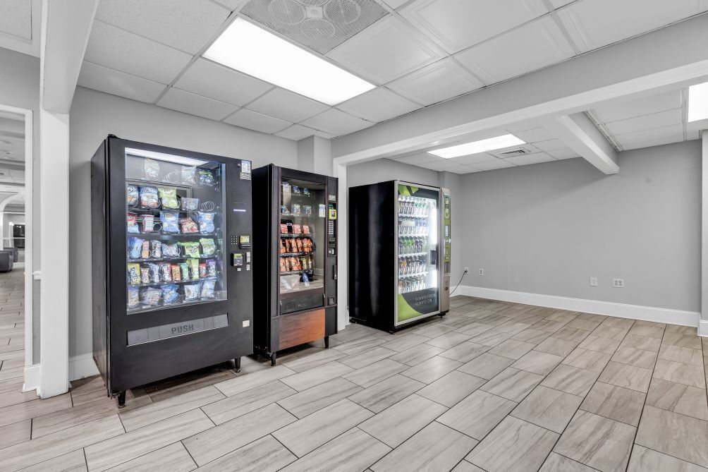 Three vending machines in a room with tiled flooring and white walls.