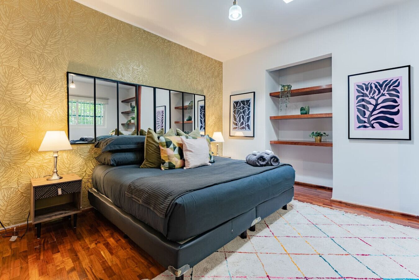 A modern bedroom with a large bed, bedside tables, a mirror, and artwork on the walls.