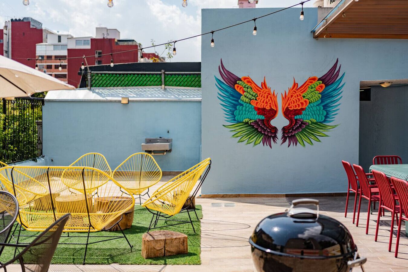 An outdoor patio with yellow chairs, a grill, and a mural of colorful wings on the wall.