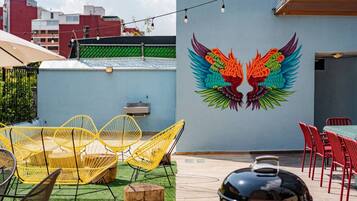 An outdoor patio with yellow chairs, a grill, and a mural of colorful wings on the wall.