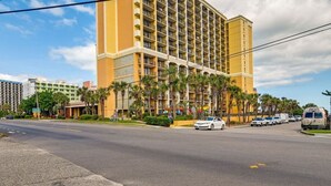 Un hotel de varios pisos con fachada amarilla, situado en una esquina con palmeras y cielo despejado.