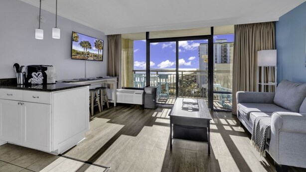 Una habitación de hotel moderna con cocina, un balcón con vistas a la ciudad y una sala de estar con sofá y mesa.