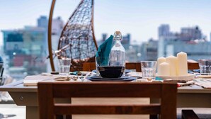 A table set for dining with a bottle, glasses, and candles, overlooking a cityscape.