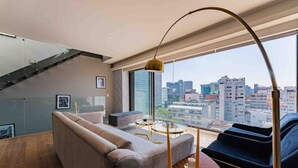 A modern living room with a sofa, a coffee table, and a view of a cityscape through large windows.
