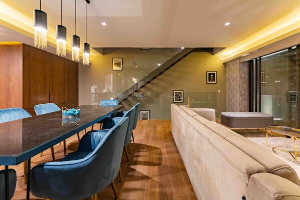 A modern dining area with a long table, blue chairs, and hanging pendant lights.