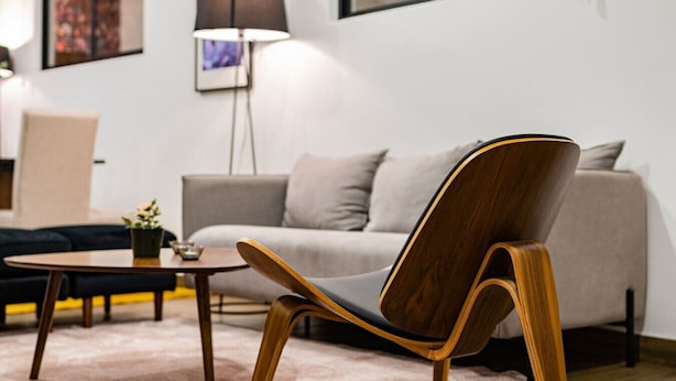 Un salon moderne avec un fauteuil en bois, un canapé gris et une lampe sur pied.
