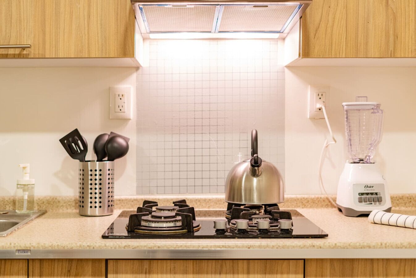 Cozinha com fogão a gás, chaleira, liquidificador e painel de fundo com padrão quadriculado.