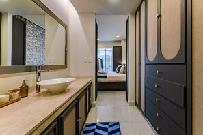 Een moderne badkamer met een grote spiegel, een witte wastafel en een inloopkast met donkere kasten.