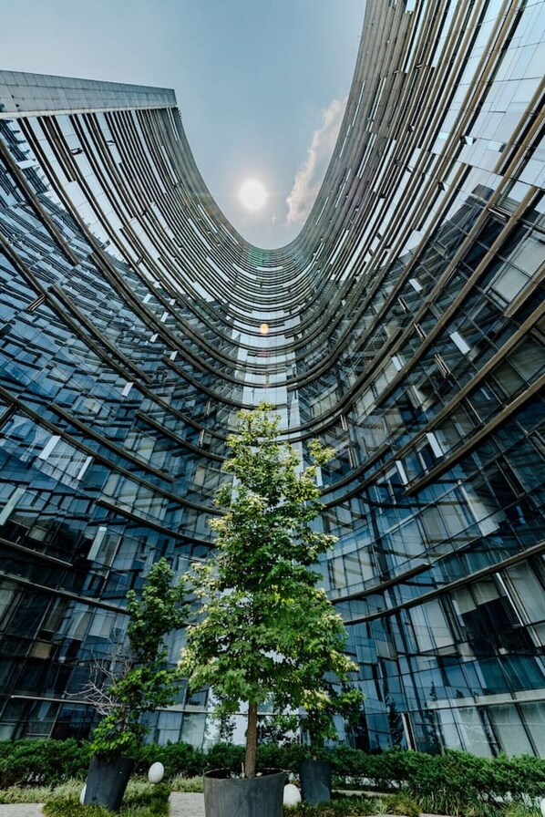 A modern building with a curved glass facade and a central tree.