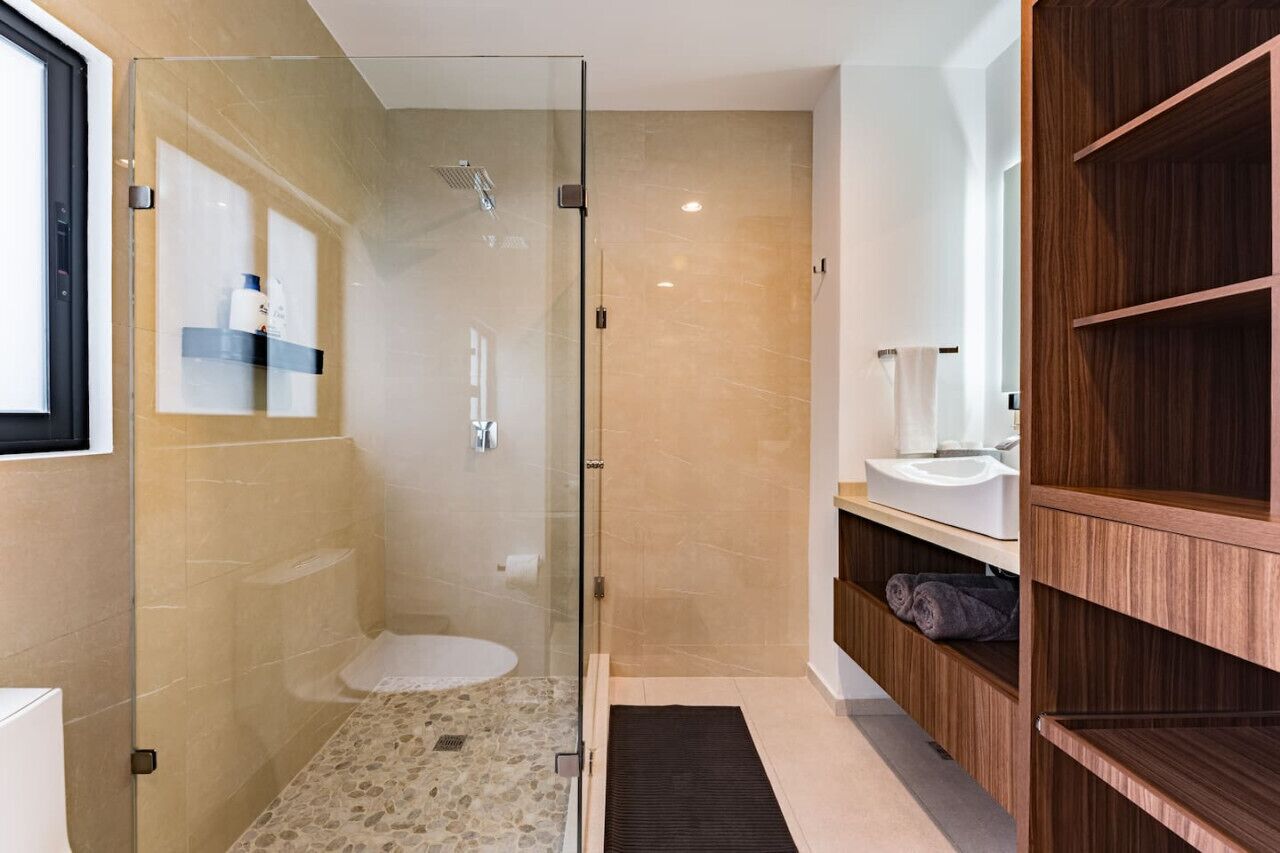A modern bathroom with a glass-enclosed shower, a white sink, and wooden shelving.