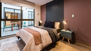 Une chambre moderne avec un grand lit, des tables de chevet, un bureau et une vue dégagée sur l’extérieur grâce à une grande fenêtre.