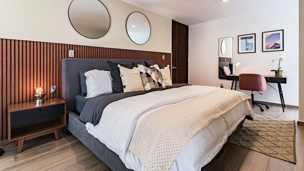 A modern bedroom with a large bed, bedside tables, a desk, and two wall-mounted mirrors.