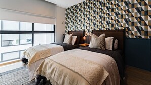 A modern hotel room with two beds, a geometric patterned wall, and a large window providing natural light.