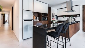 Una cocina moderna con una isla central, taburetes negros tipo barra y una campana extractora de acero inoxidable.