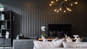A modern living room with a large flat-screen TV, a dark wood-paneled wall, a grey sofa, a wooden coffee table, and a unique ceiling light fixture. - Stylish Polanco Duo Steps from Lincoln Park (Ciudad de México)