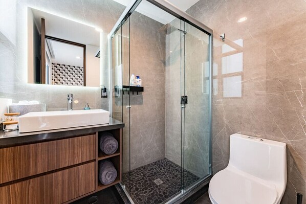 A modern bathroom with a glass-enclosed shower, a white sink, and a toilet.