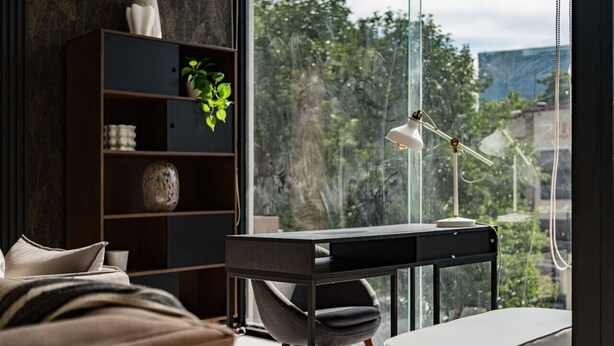 Un dormitorio moderno con un ventanal grande, un escritorio, una silla, una estantería y una cama.
