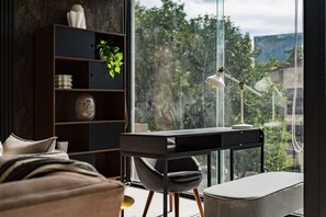 A modern bedroom with a large window, a desk, a chair, a bookshelf, and a bed.