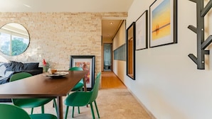 Un'area pranzo moderna con parete in mattoni, sedie verdi, tavolo in legno e opere d'arte incorniciate al muro.