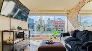 Un soggiorno moderno con un'ampia finestra, una TV a schermo piatto, un divano in pelle nera e un tavolino da caffè.