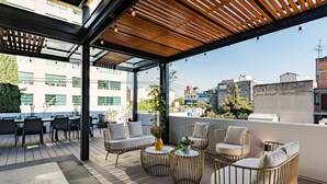 Una terraza en la azotea con mobiliario exterior, un pérgola y vistas a la ciudad.
