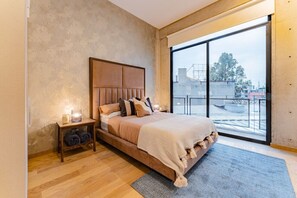 Een slaapkamer met een groot bed, een nachtkastje, een lamp en uitzicht buiten door een groot raam.