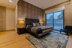 Een slaapkamer met een groot bed, twee bedlampen, een donker hoofdeinde, een groot raam en een balkon.