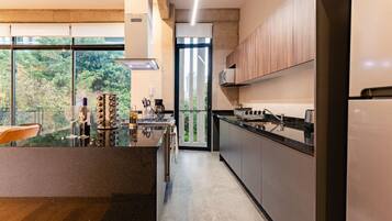 Cozinha moderna com ilha de vidro, eletrodomésticos de aço inoxidável e vista para o verde lá fora.
