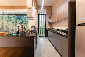 A modern kitchen with a large island, a view of greenery outside, and a sliding glass door leading to a balcony.