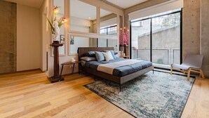 A modern bedroom with a large bed, a wooden floor, a large window, and a view of the outside.