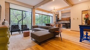 A spacious living area with large windows, a modern kitchen in the background, and a chandelier.